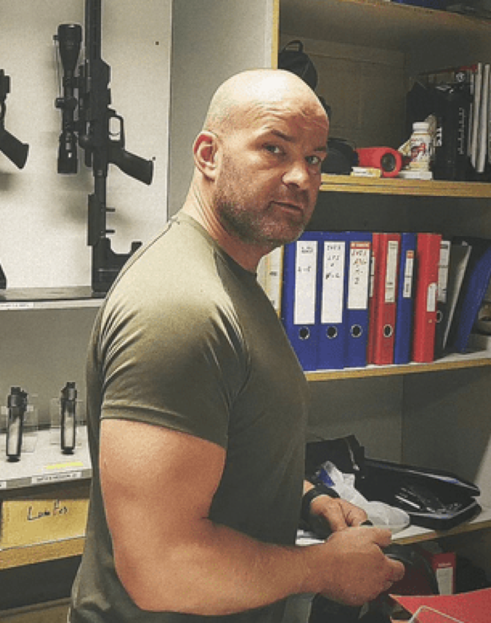 Danny, patron du Gun Club, devant le râtelier d'armes du stand